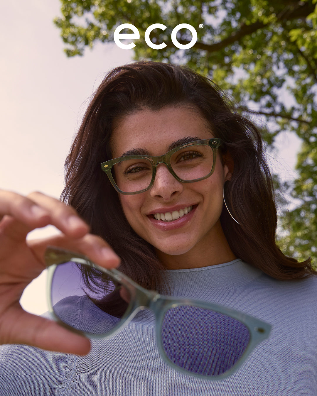 Eco Eyewear campaign featuring female model in green Biobased eyeglasses holding the matching sun clip-on in outdoor settings – sustainable women’s eyewear fashion photography.