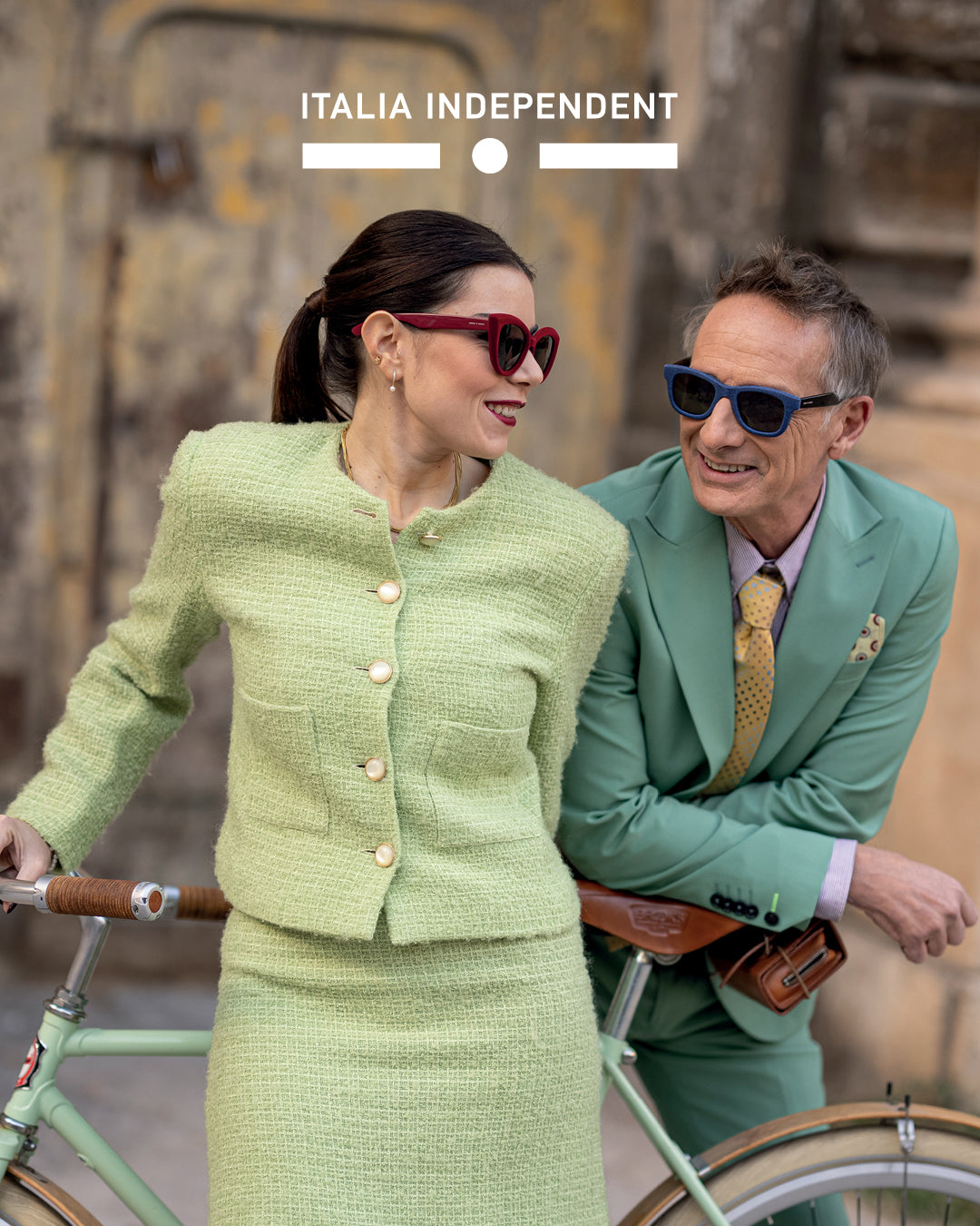 Italia Independent eyewear campaign with male and female models wearing sunglasses, leaning on a bike in urban city setting – luxury men’s and women’s sunglasses fashion photography.