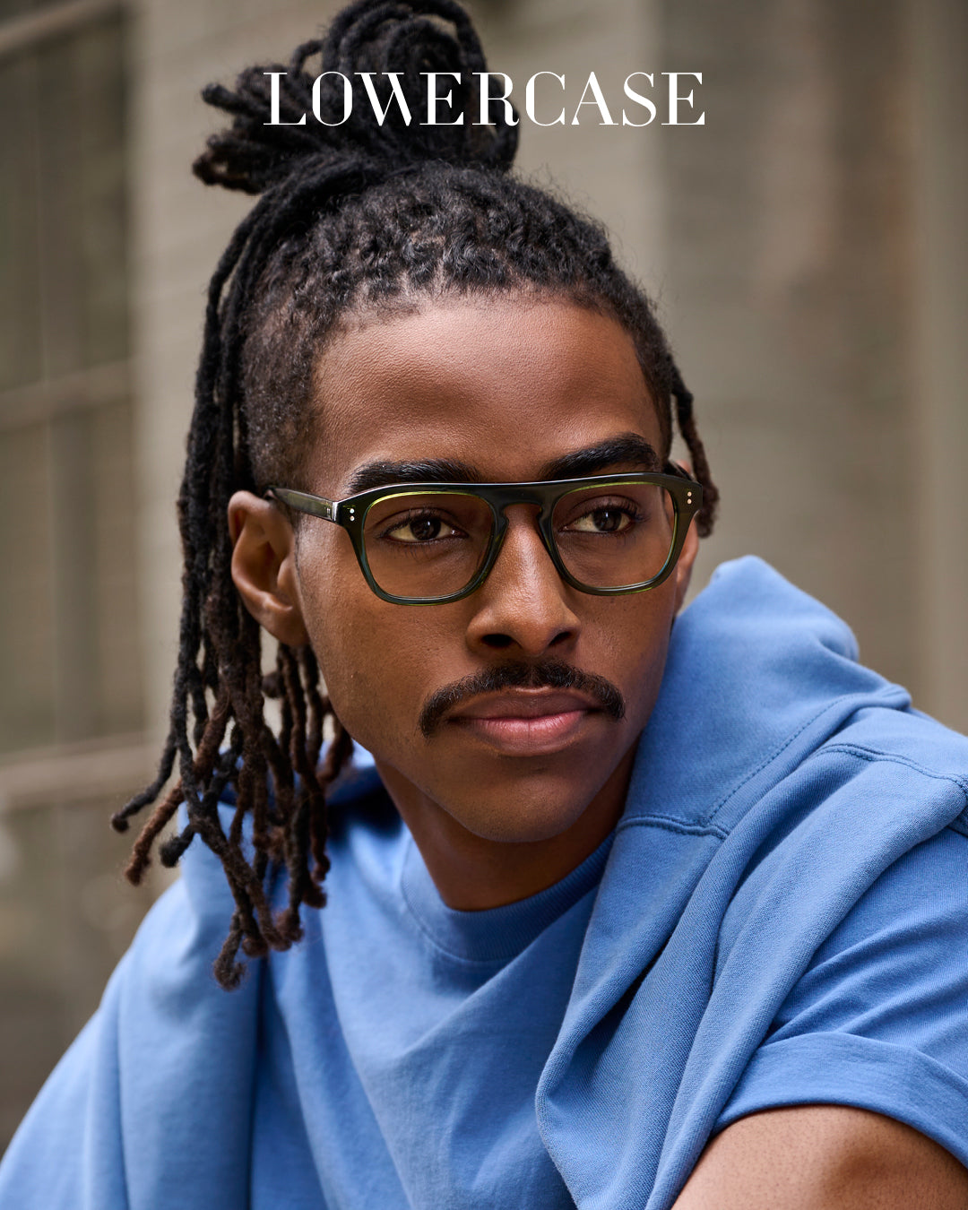 LOWERCASE Eyewear campaign featuring male model in green acetate eyeglasses with blurred urban background – luxury men’s eyewear fashion photography.