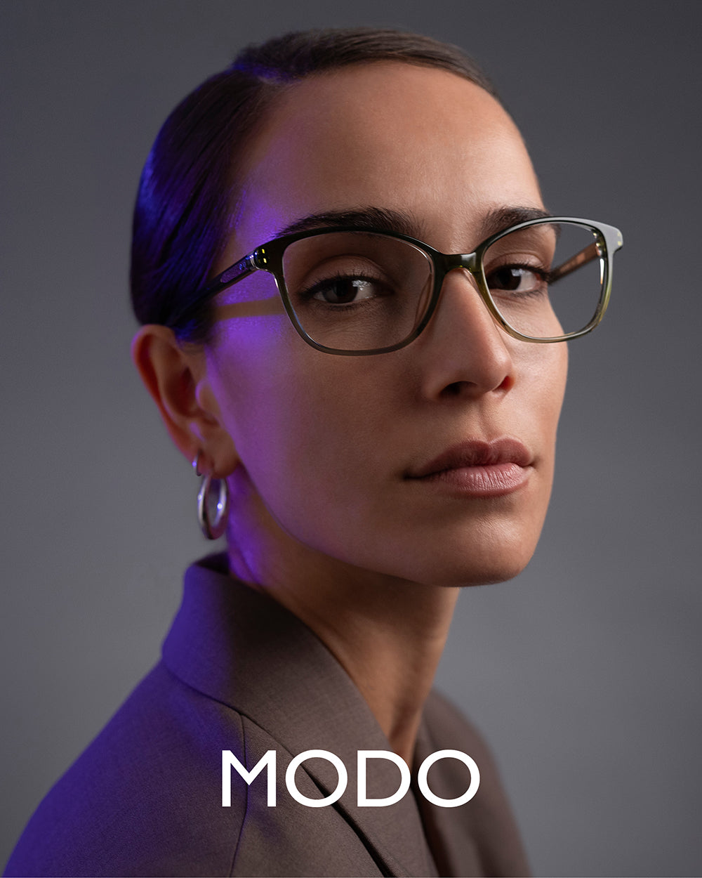 MODO Eyewear campaign featuring female model in green acetate eyeglasses with plain grey background – luxury women’s eyewear fashion photography.