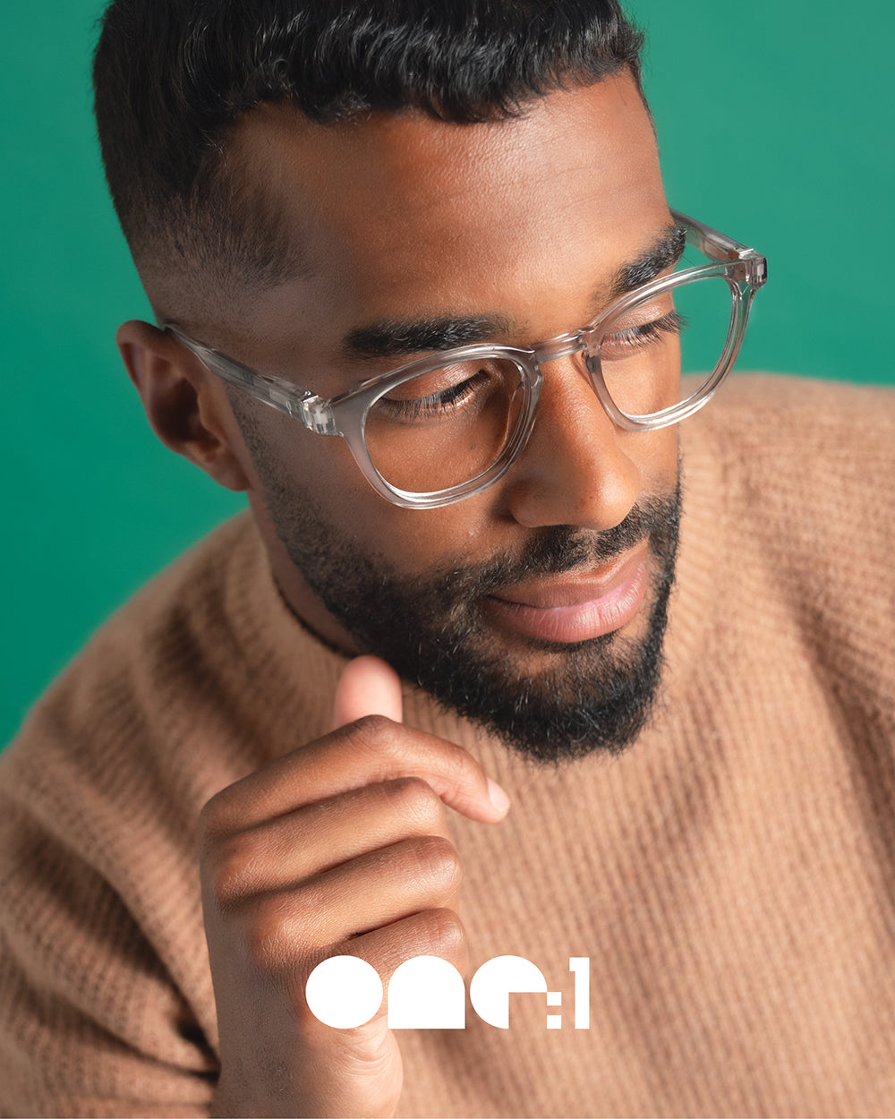 One:1 Readers campaign close-up of male model wearing clear-colored recycled plastic eyeglasses against green plain background – sustainable luxury eyewear fashion photography.