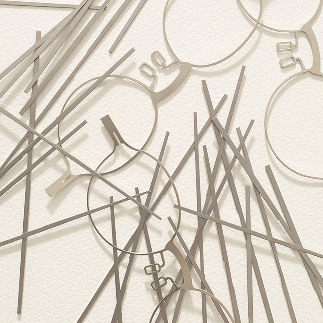 Titanium eyewear front cutouts and titanium pieces casually arranged on a flat surface.