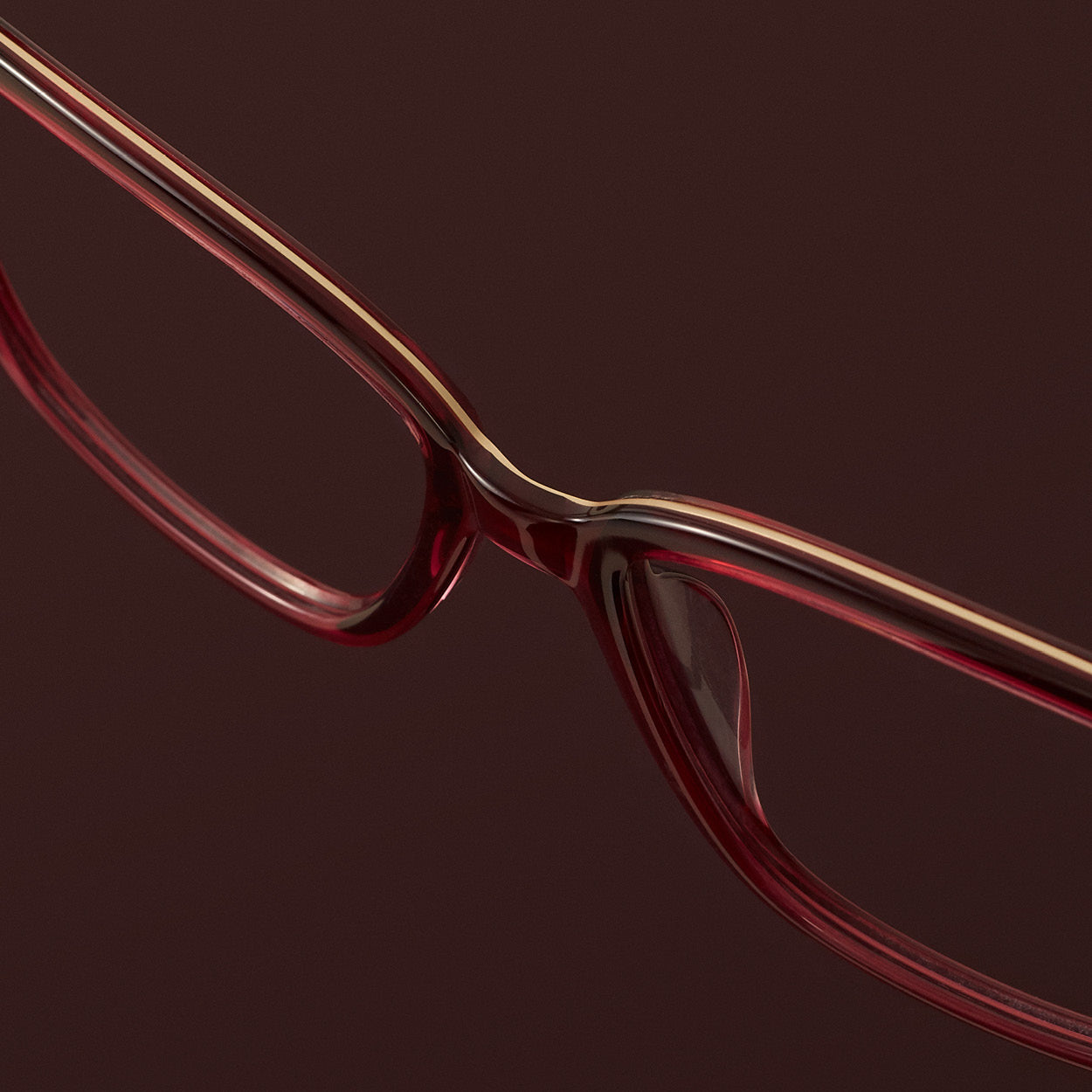 Close-up of red eyeglass frame with layered materials on dark red background – modern eyewear design detail.