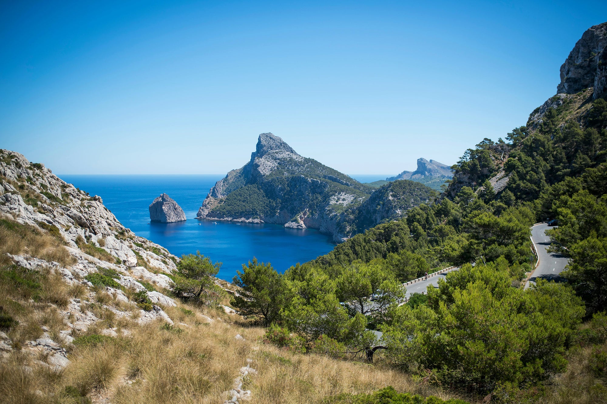 Bright coastal landscape with sea, green hills, and a winding road—viewed with the natural eye protected from polarized and high chromatic definition lenses.