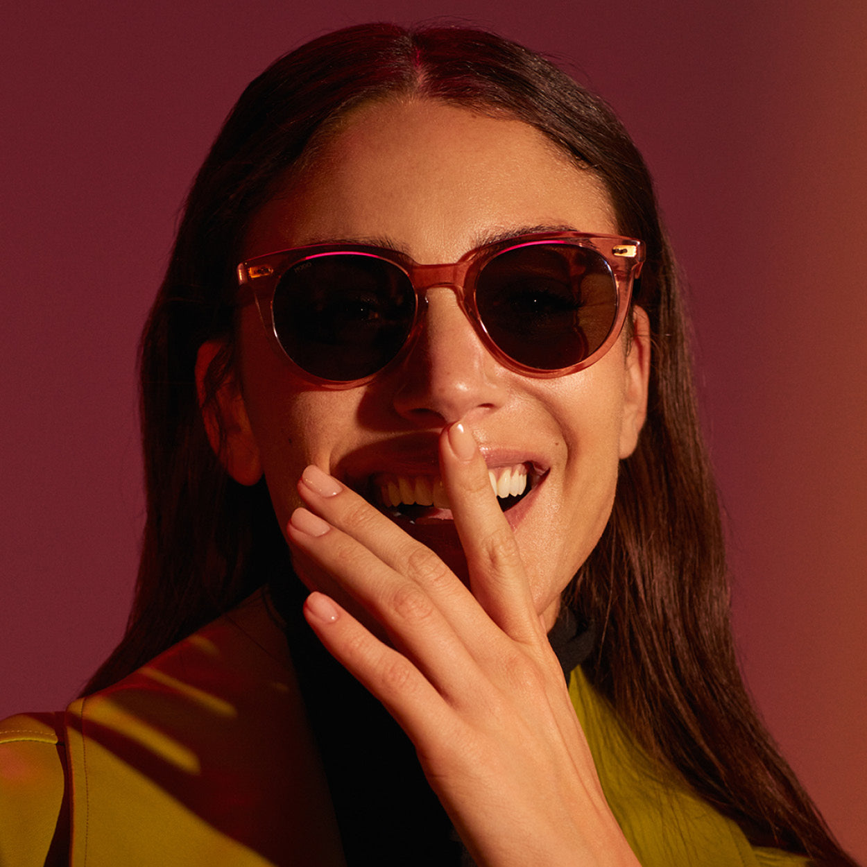 Close-up of a smiling female model wearing MODO Eyewear sunglasses, with her hand playfully covering part of her mouth.