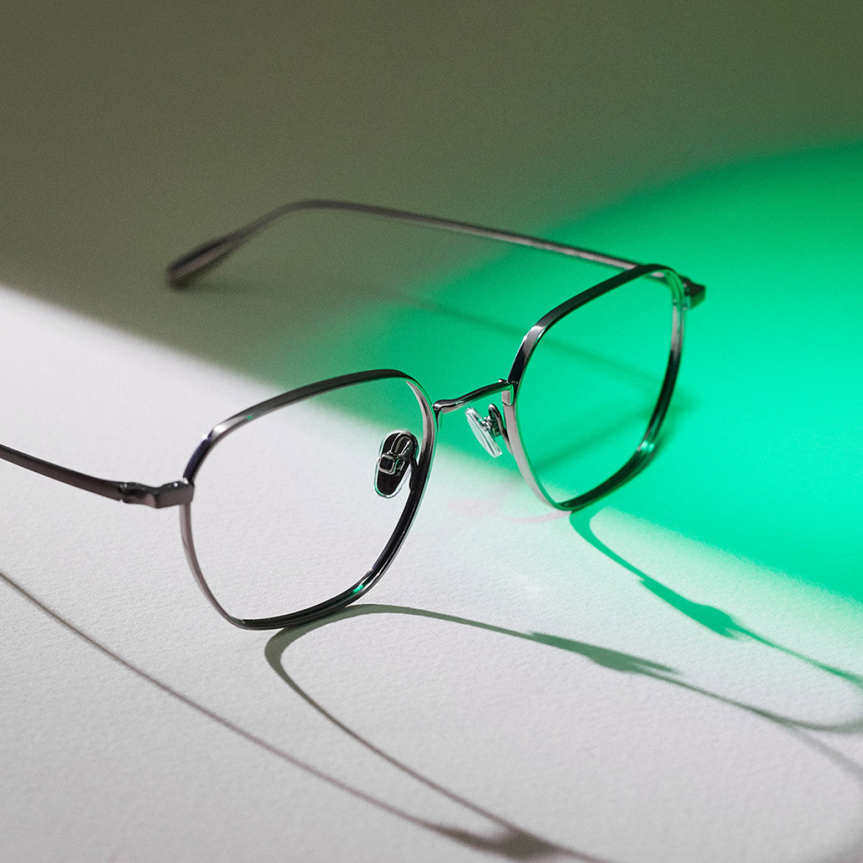 Still life photo of a silver metal eyeglass frame with green backlighting – luxury eyewear still life photography.