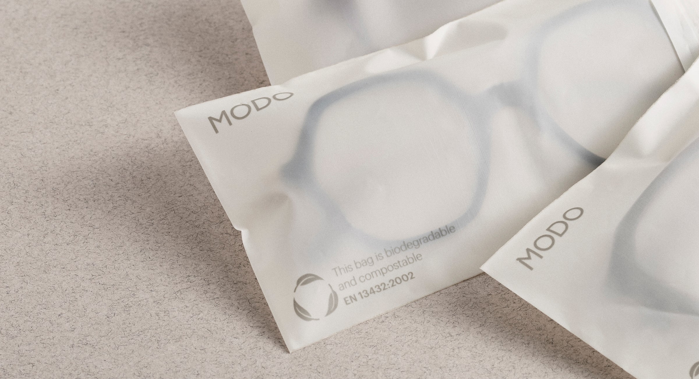 Flatlay of three MODO Eyewear cornstarch packaging bags, each containing an eyeglass frame—highlighting sustainable eyewear packaging.